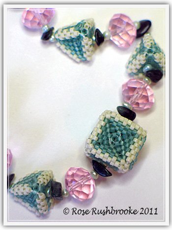 Close up of Triangles and Squares necklace by Rose C Rushbrooke. Seafoam and cream beaded beads, pale blue dyed pearls, green opal chips, pink rondelles glass beads, and mint pressed glass beads. Peyote stitch beadweaving. Image copyright &copy; Rose C Rushbrooke.
